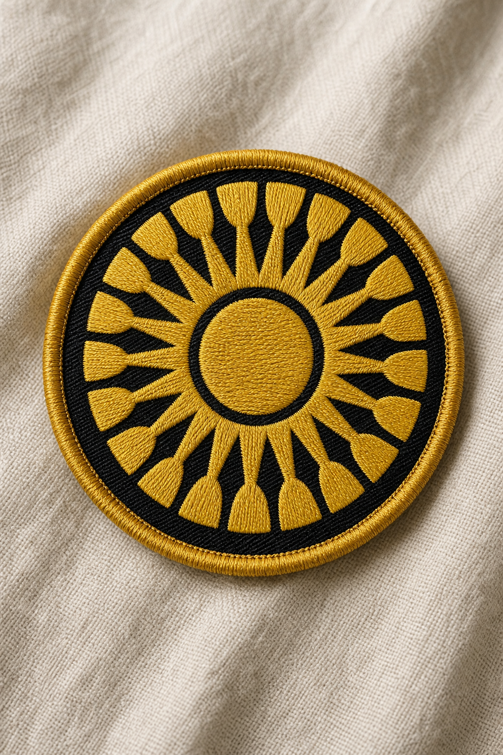 Round embroidered patch of the AoIK sun emblem in golden thread